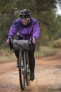 Woman in protective helmet and colorful jacket riding bikes in forest during bike packing adventure