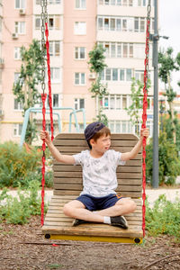 Little boy riding a swing in a green park. happy childhood. a boy rides on a wide swing, close-up.