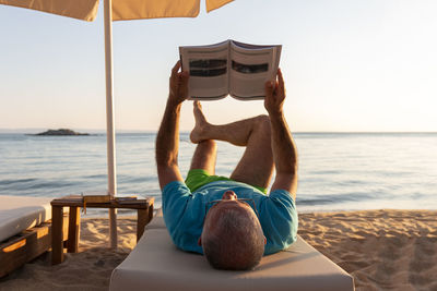 Mature man lying on a sunbed and reading a book at sunset. summer vacation concept.