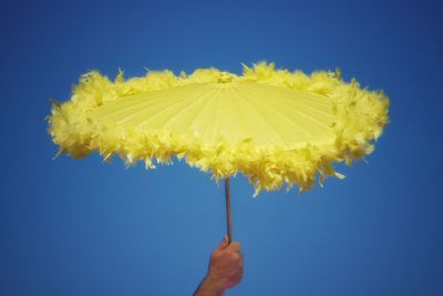 Cropped hand of man holding yellow umbrella against clear blue sky