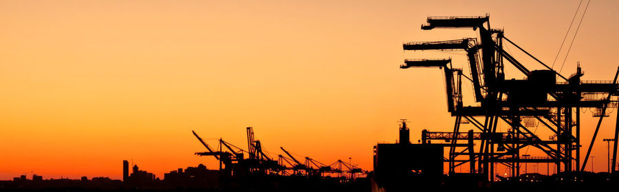 Silhouetted cranes against sky at sunset