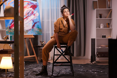 Young woman holding paintbrush sitting on chair