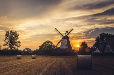 Traditional windmill on field against sky during sunset