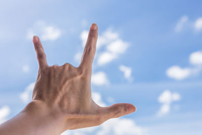 Low angle view of hand gesturing against sky