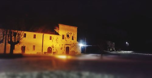 Illuminated buildings by street against sky at night