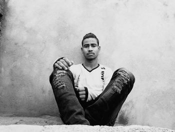 Young man sitting against wall