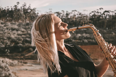 Beautiful woman playing saxophone against tree