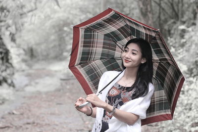 Happy young woman holding umbrella while standing in forest