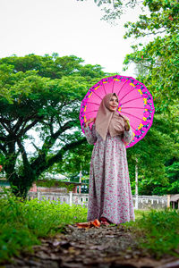 Woman holding umbrella standing by tree during rainy season