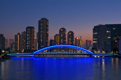 Illuminated city by river against sky at night