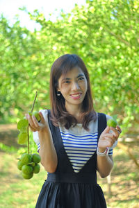 Portrait of smiling woman holding lemons against trees