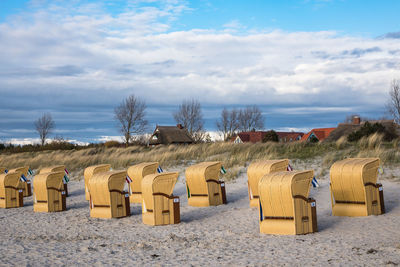 Hooded chairs on beach against sky