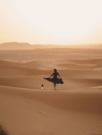 Rear view of woman dancing by lantern at sahara desert against sky during sunset