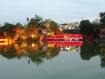 Illuminated city by river against sky at night