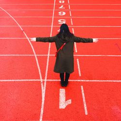 Full length of woman with arms outstretched standing on running track
