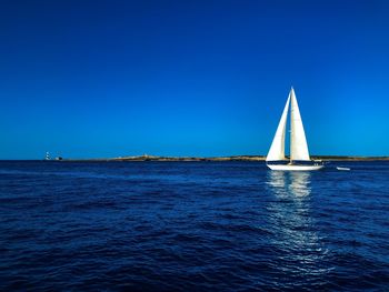 Sailboat sailing in sea against clear blue sky