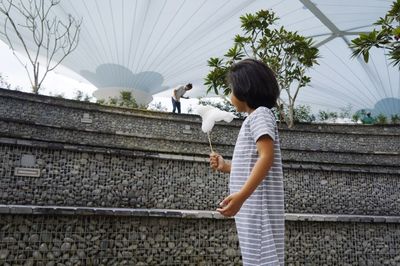 Side view of girl standing by retaining wall against sky