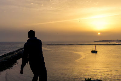 Silhouette man fishing on beach against sky during sunset