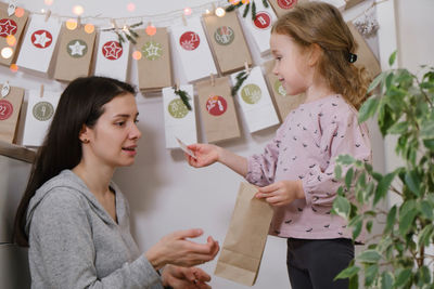 Mother with child opening christmas advent calendar tasks and gifts. toddler girl excited 