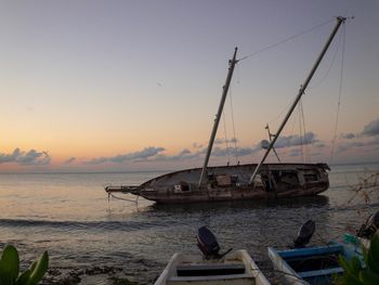 Sailboats moored on sea against sky during sunset