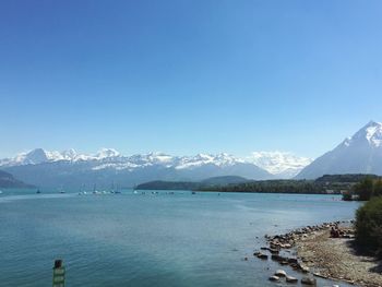 Scenic view of sea and mountains against clear blue sky