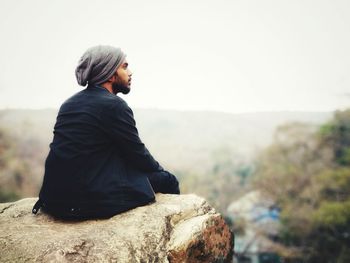 Man sitting on rock against sky