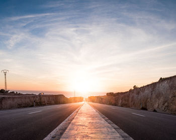 Road leading towards city against sky during sunset