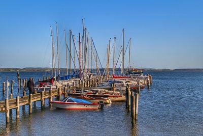 Sailboats moored by pier in river against sky on sunny day