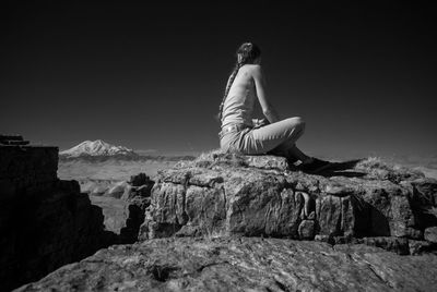 Woman sitting on rock against sky