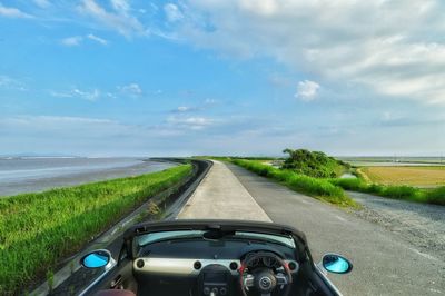 Car on road amidst field against sky