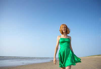 Rear view of woman standing at beach against clear sky