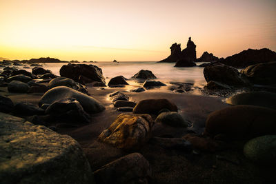 Rocks on beach against sky during sunset