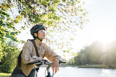 Thoughtful woman with bicycle in park on sunny day