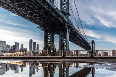 Low angle view of manhattan bridge by buildings against sky in city during sunny day