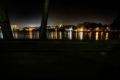 Illuminated buildings by river against sky at night