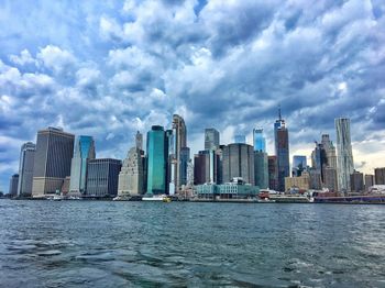 Sea and buildings in city against cloudy sky