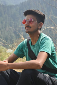 Young man looking away while sitting on land