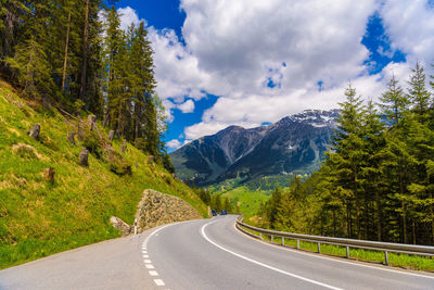 Road amidst trees and mountains against sky