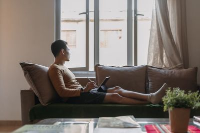 Young woman using laptop while sitting on bed at home