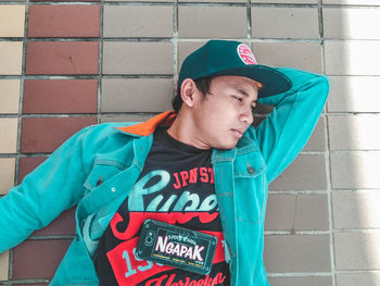 Young man looking away while standing against wall