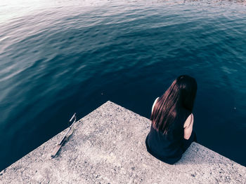 High angle view of woman sitting on pier over sea