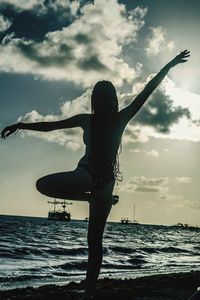 Woman with arms raised on beach against sky during sunset