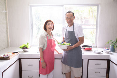 Portrait of smiling senior couple preparing food in kitchen