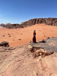 Man standing on rock in desert against clear sky