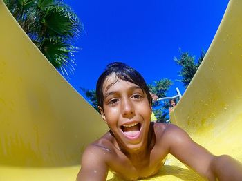 Close-up portrait of cheerful shirtless boy sliding on water slide