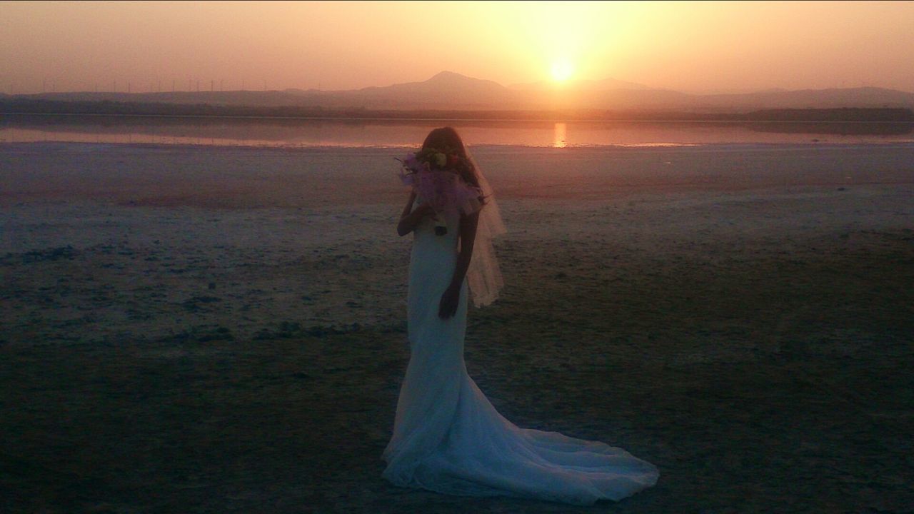 sunset, sun, water, tranquility, tranquil scene, beauty in nature, scenics, sunlight, standing, nature, sea, idyllic, full length, beach, sunbeam, sky, rear view, orange color