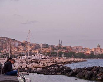 Man sitting on rock by sea against sky