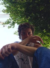 Portrait of young man sitting against tree