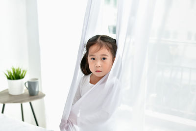 Portrait of cute girl standing behind curtain at home