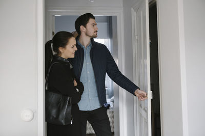 Young man opening door while standing with woman in corridor at home